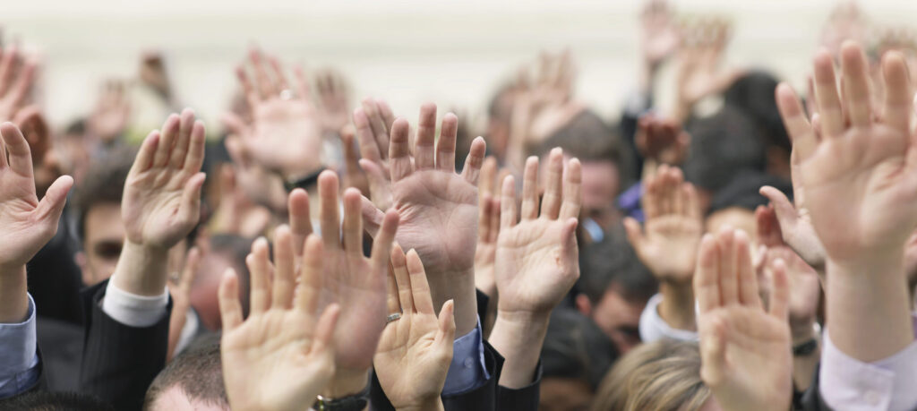 Crowd of people with hands raised to volunteer